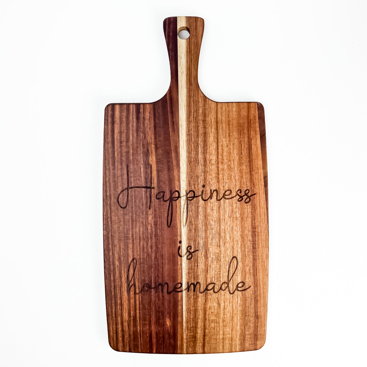 Wooden cutting board with 'Happiness is homemade' engraving on a white background. Acacia wood laser engraved charcuterie board and serving board handmade in Spain 