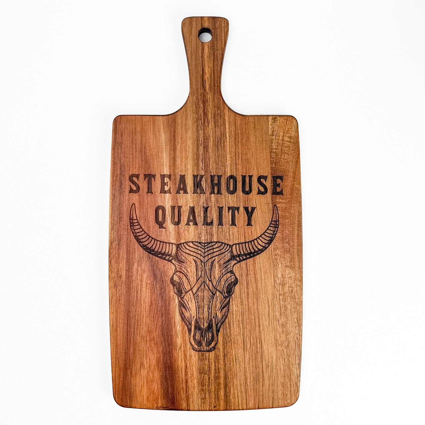 Wooden cutting board with a bull skull design and 'Steakhouse Quality' text on a white background. Acacia wood laser engraved charcuterie board and serving board handmade in Spain 